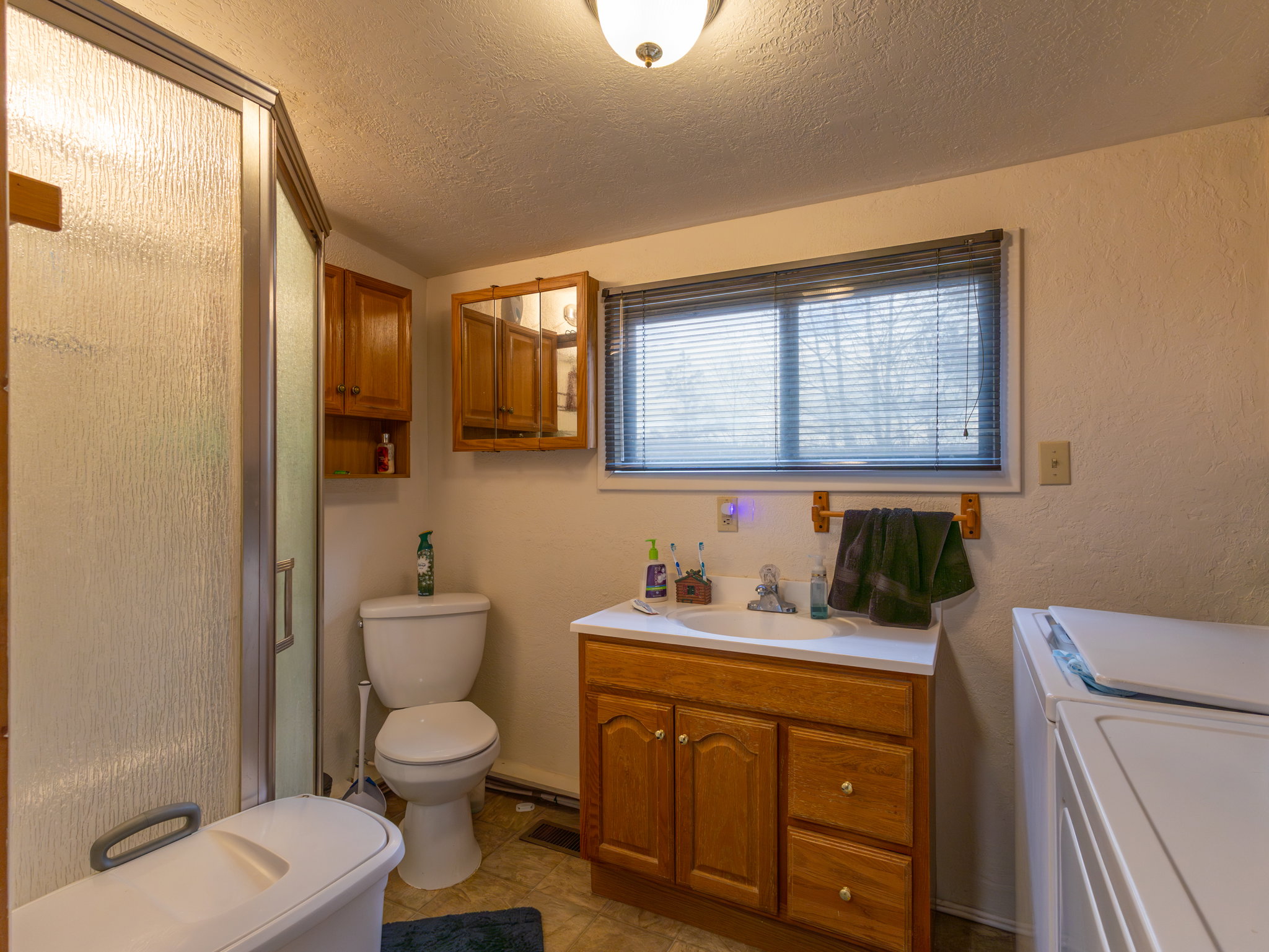 Bathroom featuring a glass-enclosed shower, a vanity with wood-finish cabinetry, a window with blinds, and tile flooring