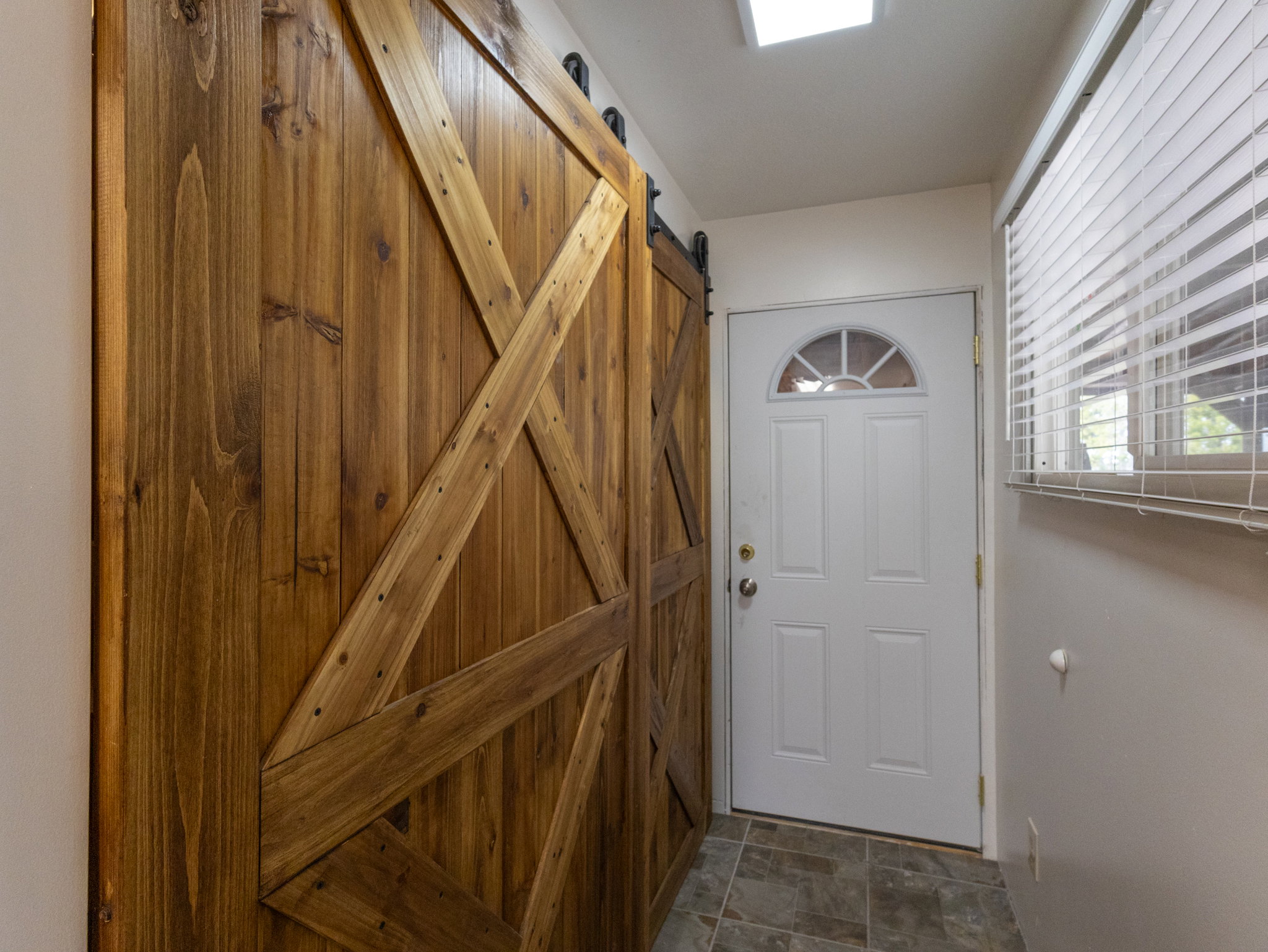 Rustic wood barn door with black hardware, complementing the white exterior door with an arched window