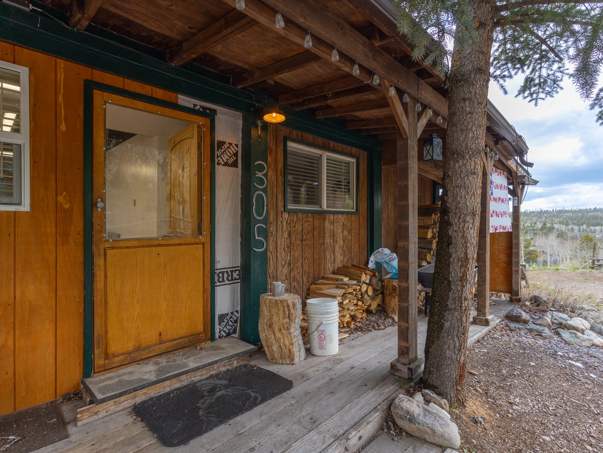 Rustic wood siding with a covered porch featuring exposed wood beams, a wood plank ceiling, and a prominent tree integrated into the porch structure
