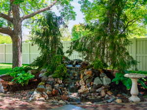 Rock waterfall feature surrounded by mature trees and lush hostas
