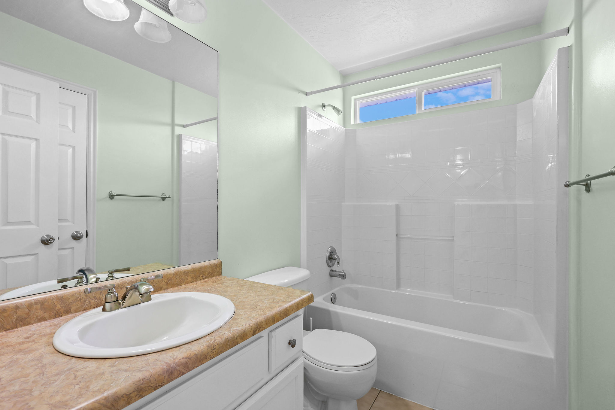 Full bathroom featuring a white tub with integrated shower, a vanity with an oval sink, a light-colored countertop, and a mirror