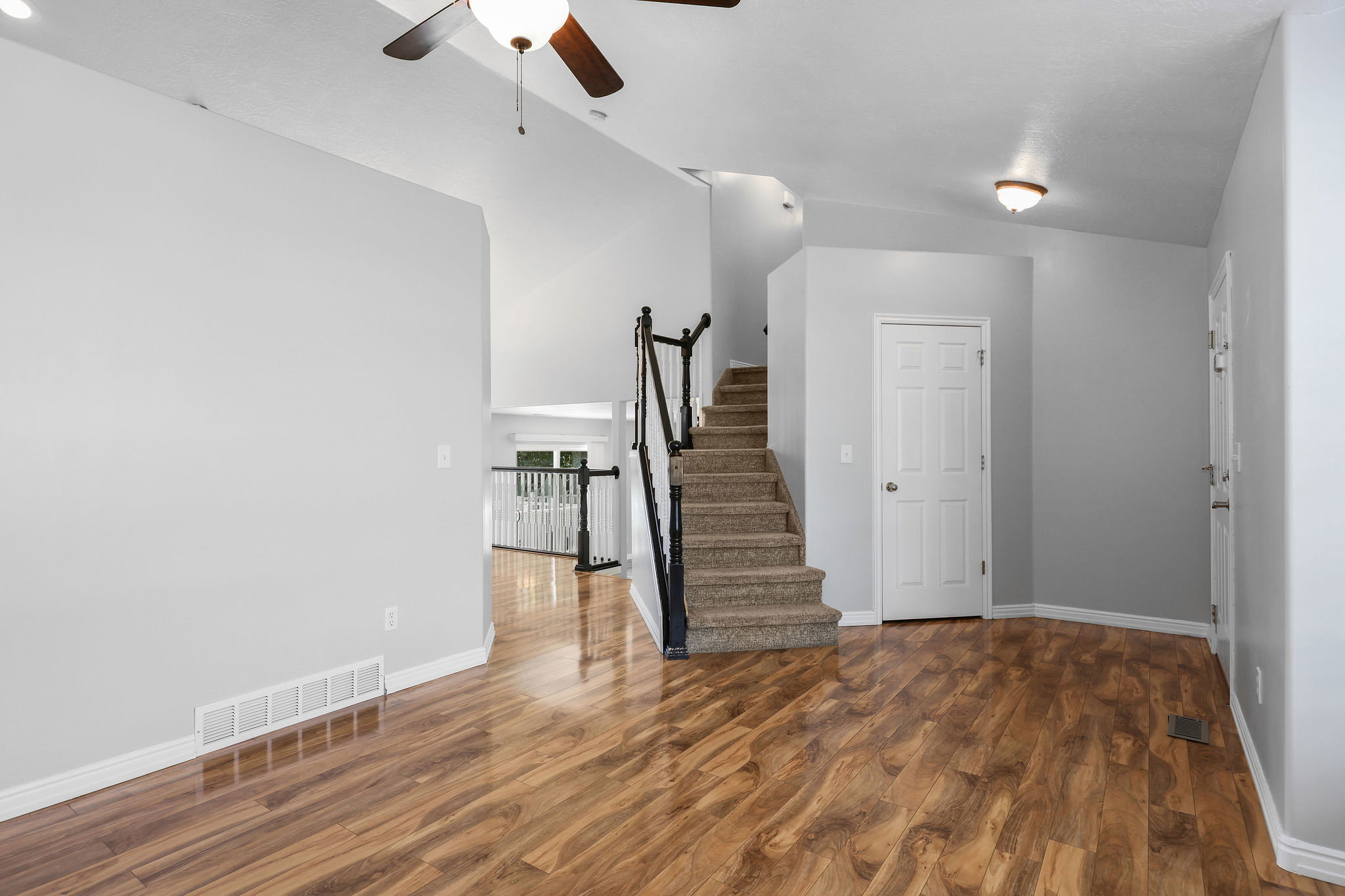Open-concept interior featuring wood-finish flooring, a carpeted staircase with dark railings, and a white paneled door