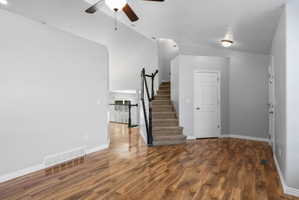 Open-concept interior featuring wood-finish flooring, a carpeted staircase with dark railings, and a white paneled door