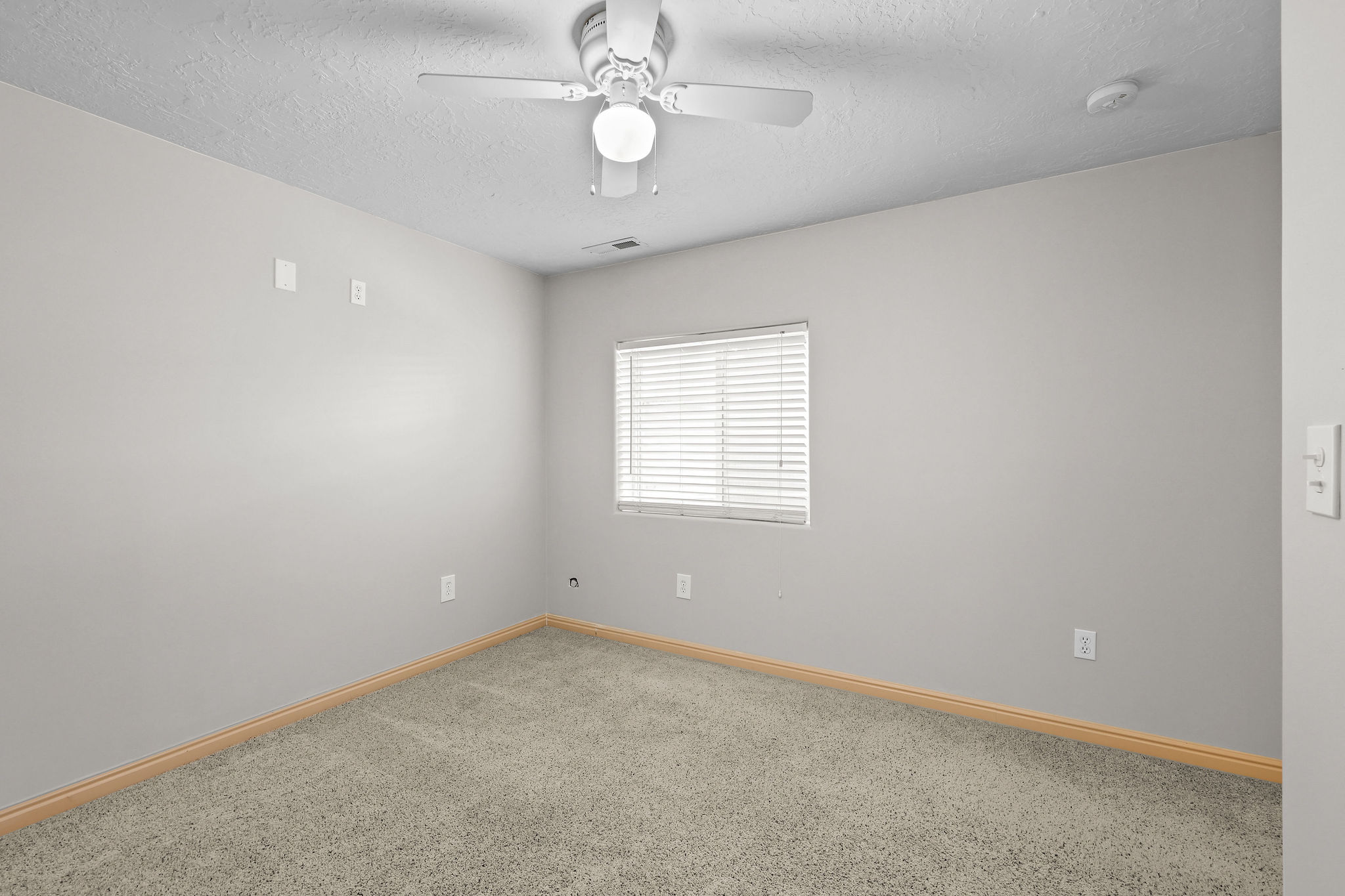 Carpeted room featuring a ceiling fan with integrated lighting, a single window with blinds, light gray wall paint, and light-toned baseboards