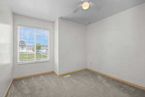 Room featuring a large window with white blinds, neutral carpeting, and a ceiling fan with integrated lighting