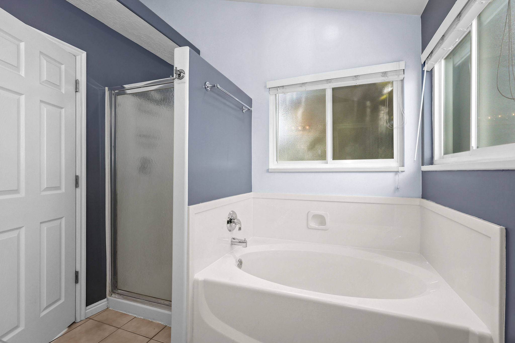Bathroom featuring a built-in corner soaking tub, separate shower with frosted glass enclosure, and white panel wainscoting