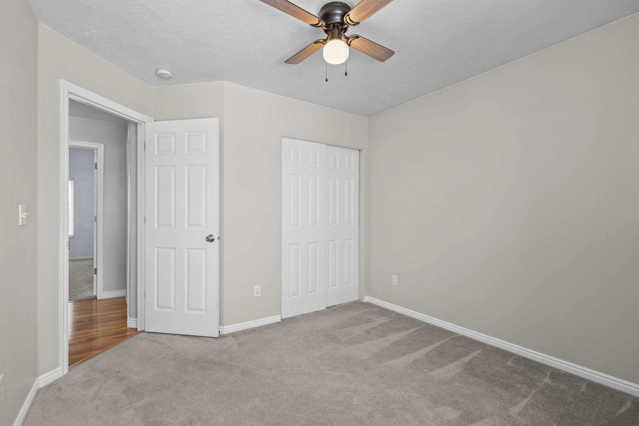 Room featuring light gray wall paint, gray carpeting, a ceiling fan with light fixture, and white bi-fold closet doors