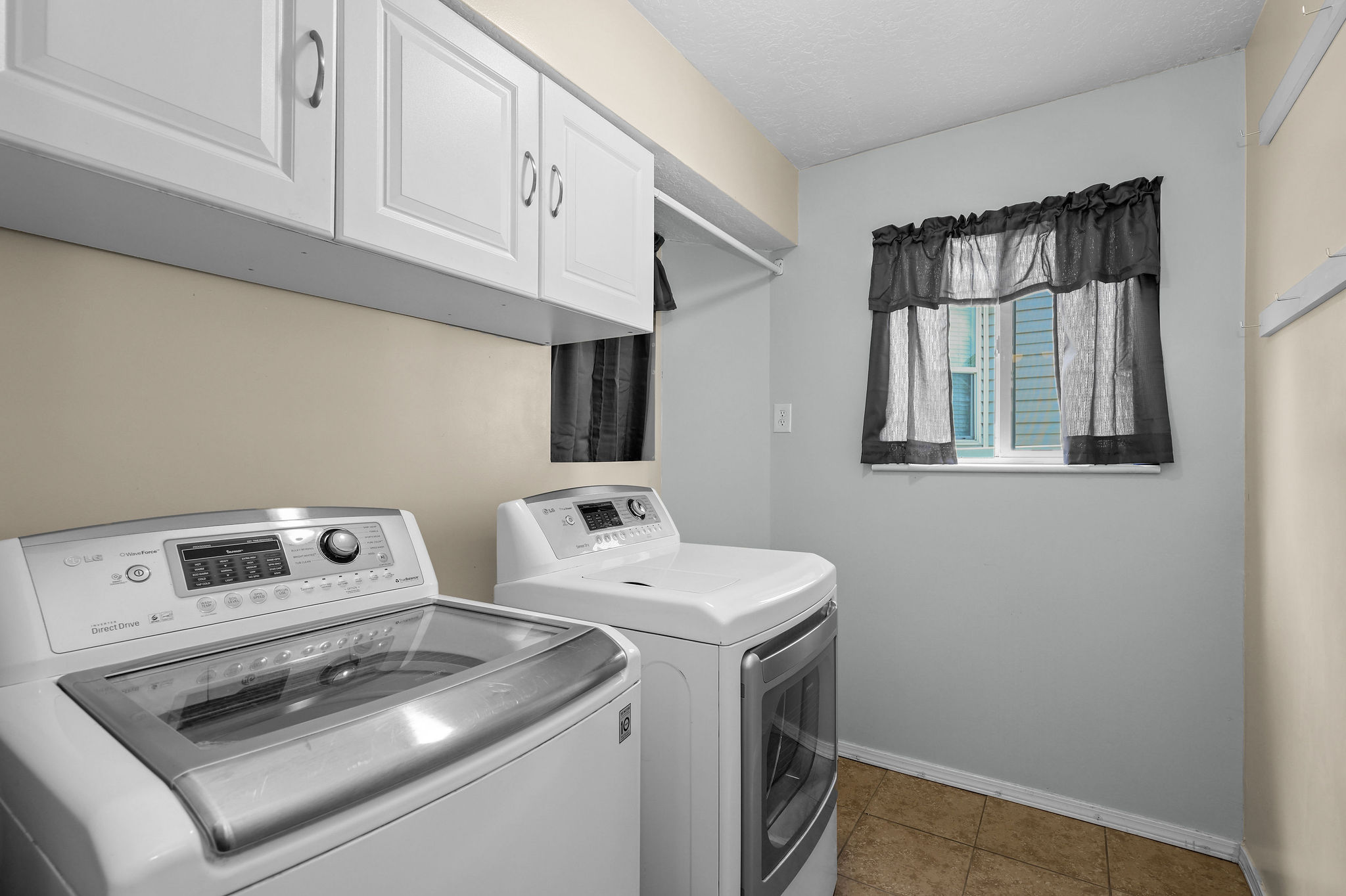 Laundry area featuring upper cabinetry, a window, and tile flooring