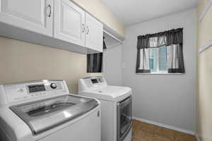 Laundry area featuring upper cabinetry, a window, and tile flooring