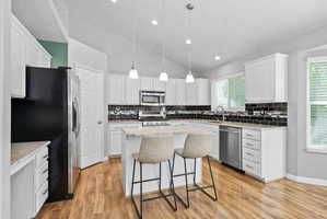 Kitchen featuring white cabinetry, wood-finish flooring, and a stone-finish island with pendant lighting