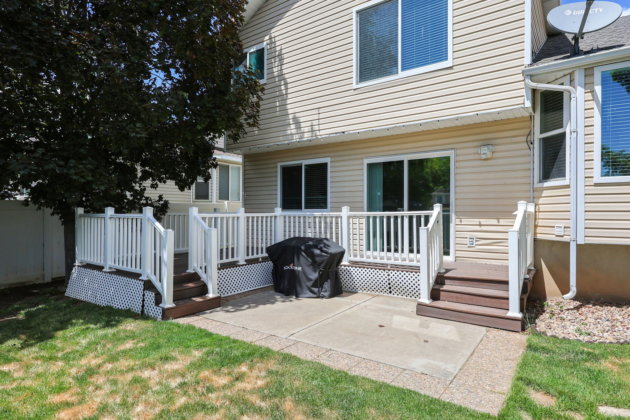 Rear exterior featuring a multi-level deck with white railings, a concrete patio, and a mature tree providing shade