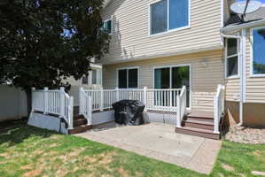 Rear exterior featuring a multi-level deck with white railings, a concrete patio, and a mature tree providing shade