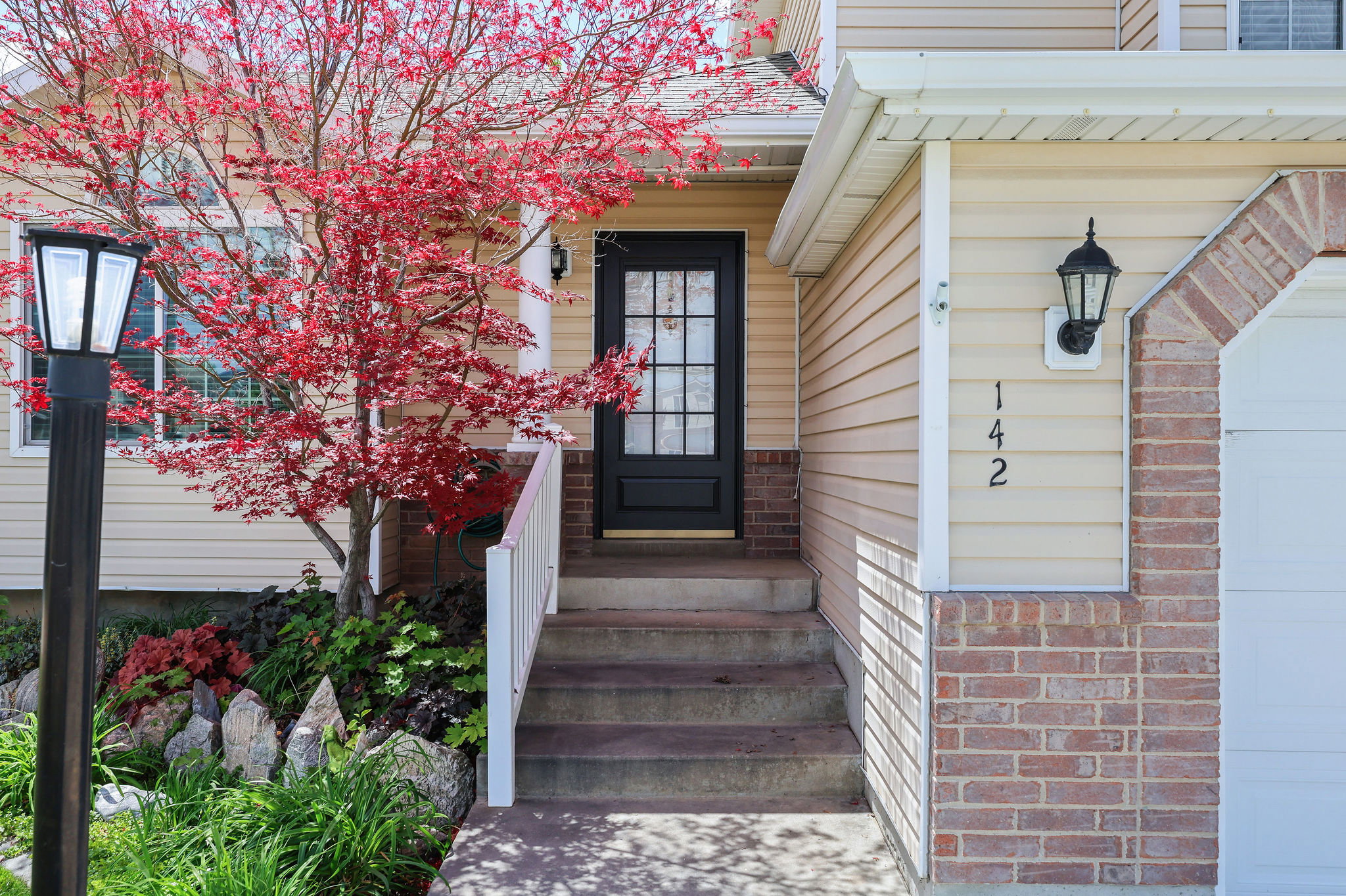 Inviting front entry featuring a black multi-pane door, concrete steps with a white railing, and a mature tree with vibrant red foliage