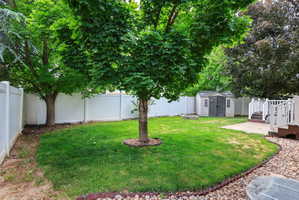 Fenced backyard featuring mature shade trees, a well-maintained lawn, a built-in fire pit, and a storage shed