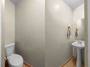 Compact powder room featuring a pedestal sink with chrome fixtures, a wall-mounted mirror, and tile flooring