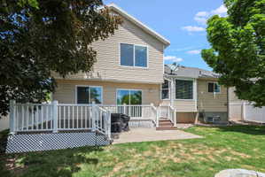Expansive backyard featuring a wood-finish deck with white railing, a concrete patio, and a verdant lawn