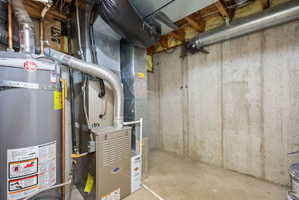 Utility area featuring a water heater, furnace, exposed ductwork, concrete flooring, and concrete foundation walls