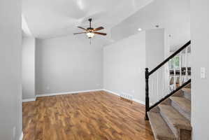 Spacious living area featuring wood-finish flooring, vaulted ceilings, and a ceiling fan with integrated lighting