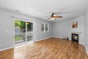 Spacious room featuring wood-finish flooring, a ceiling fan with integrated lighting, and a corner fireplace with a mantel
