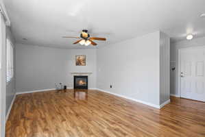 Living space featuring wood-finish flooring, a corner fireplace with a white mantel, and a ceiling fan