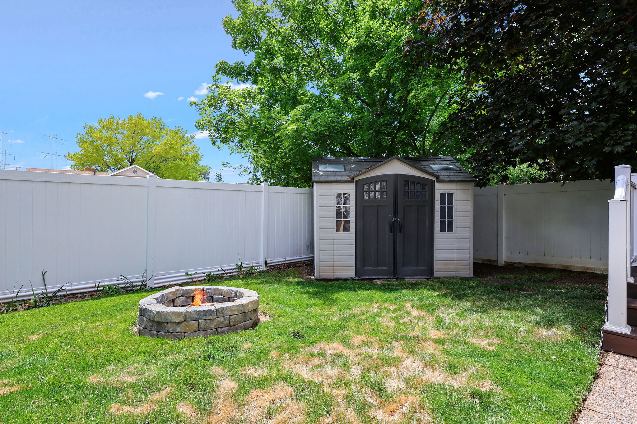 Expansive backyard featuring a stone fire pit, a vinyl privacy fence, and a utility shed with double doors and window accents
