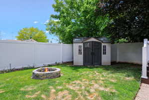 Expansive backyard featuring a stone fire pit, a vinyl privacy fence, and a utility shed with double doors and window accents