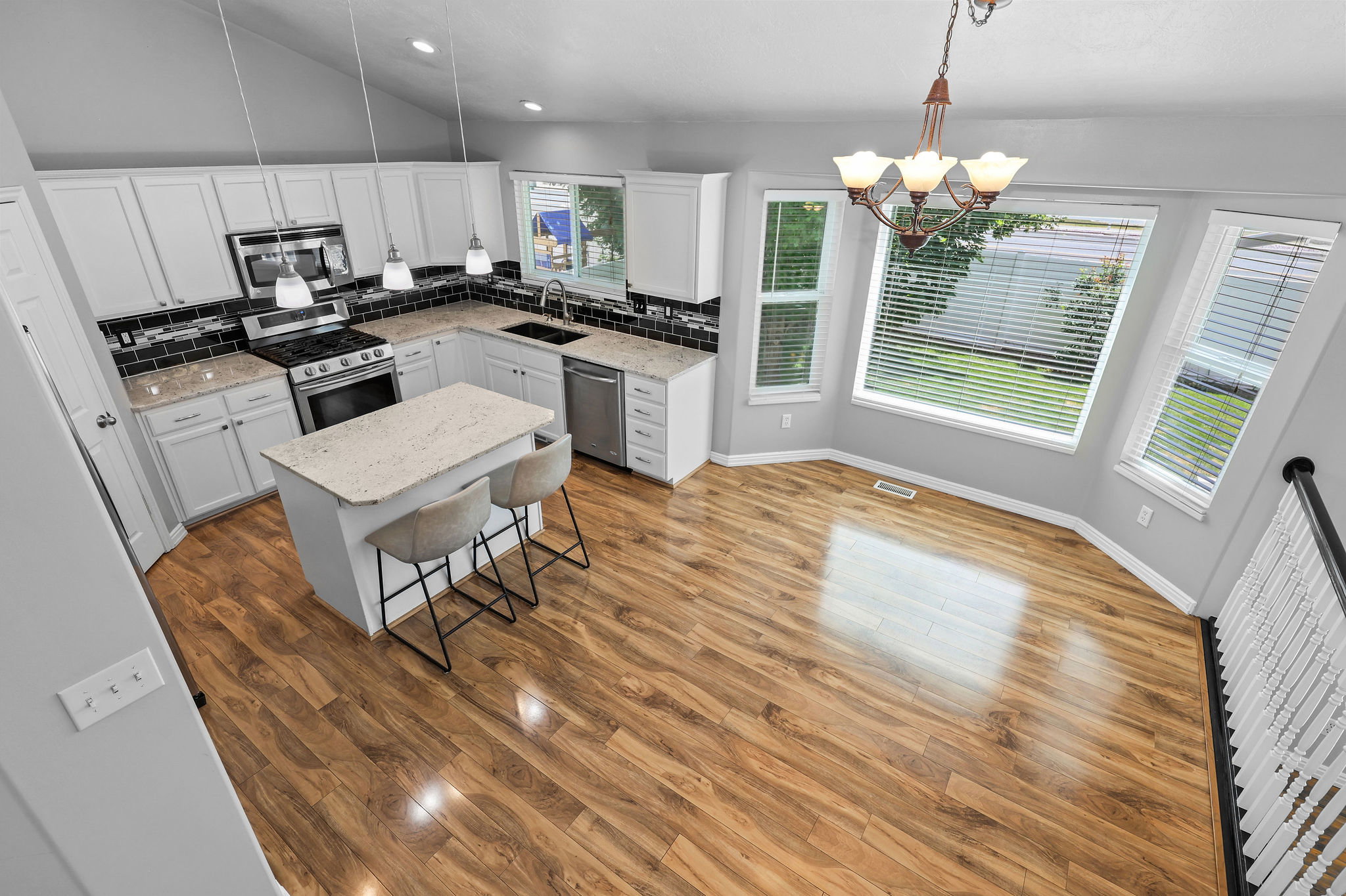 Kitchen and dining area featuring wood-finish flooring, white cabinetry, dark subway tile backsplash, and light-toned countertops