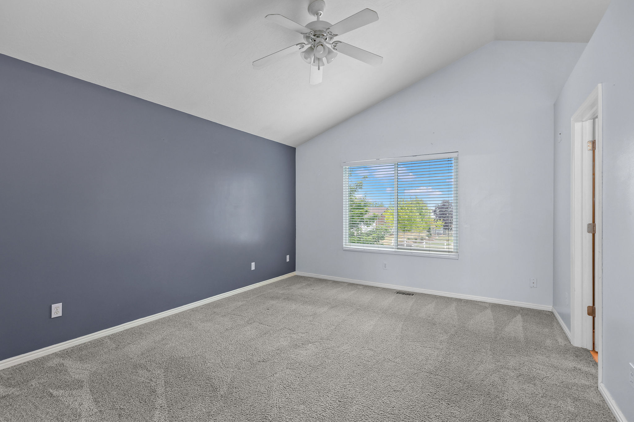 Vaulted ceiling with a white ceiling fan, gray carpeting, and a contrasting accent wall