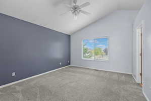 Vaulted ceiling with a white ceiling fan, gray carpeting, and a contrasting accent wall
