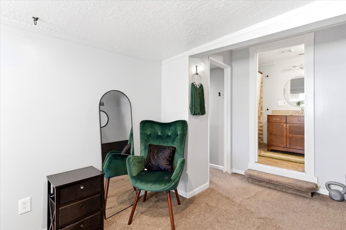 Carpeted room with a doorway opening to a bathroom featuring a wooden vanity, countertop, and a round mirror