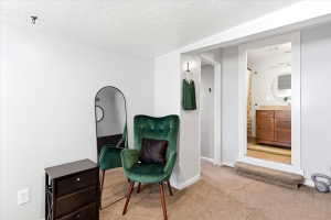 Carpeted room with a doorway opening to a bathroom featuring a wooden vanity, countertop, and a round mirror