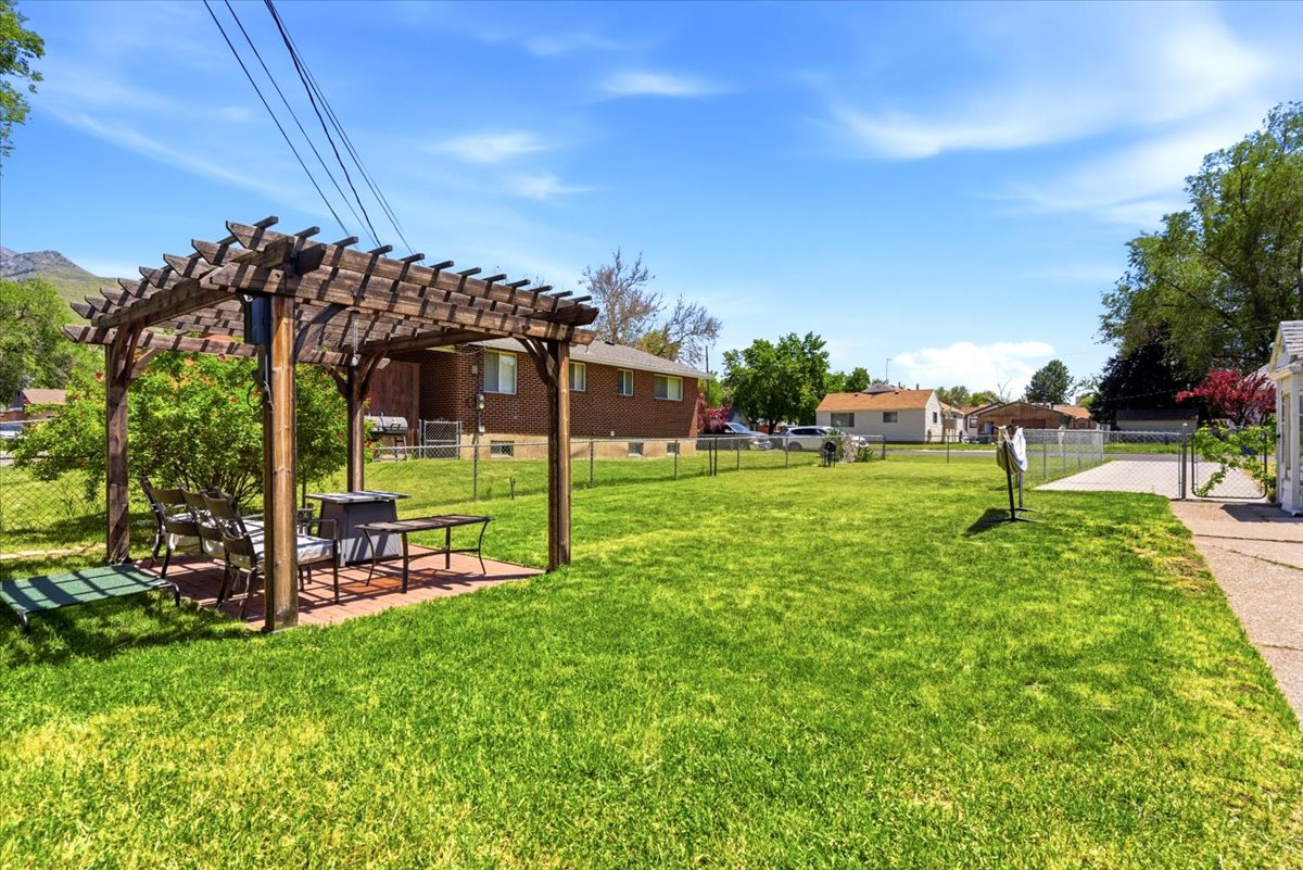 Spacious backyard featuring a wood pergola over a brick paver patio, a concrete driveway, and established trees