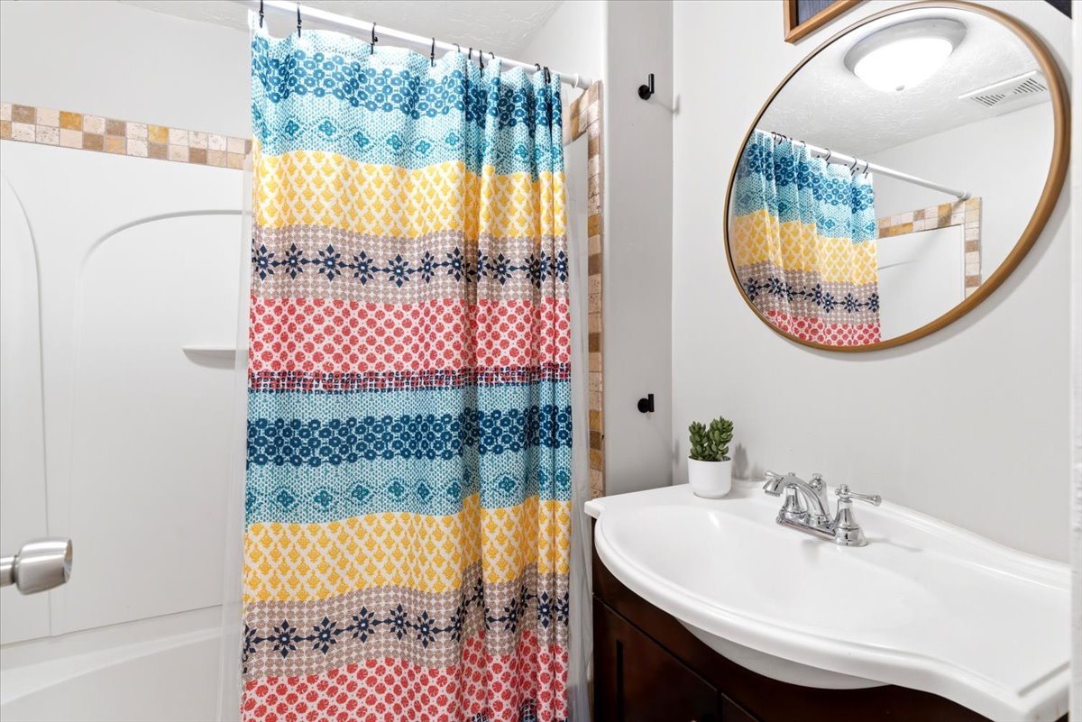 Bathroom featuring a white bathtub, tiled shower surround, dark wood vanity, integrated sink, and a round framed mirror