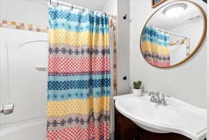 Bathroom featuring a white bathtub, tiled shower surround, dark wood vanity, integrated sink, and a round framed mirror