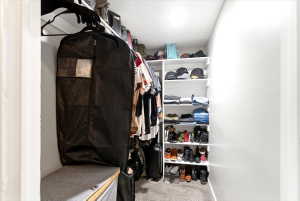 Walk-in closet featuring white built-in shelving, carpet flooring, a hanging rod, and a padded bench