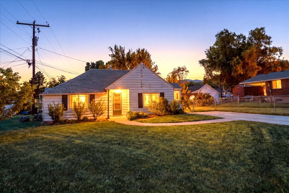 White siding exterior with dark shutters, front porch, mature landscaping, and an asphalt driveway