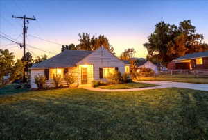 White siding exterior with dark shutters, front porch, mature landscaping, and an asphalt driveway