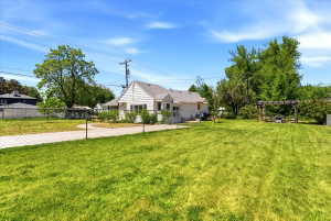 Expansive backyard featuring a large grass lawn, chain-link fencing, a stone aggregate driveway, and a wood pergola