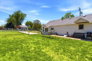 Expansive green lawn with a chain-link fence, leading to a paved drive