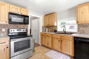 Kitchen featuring wood cabinetry, stainless steel range, black microwave, and black dishwasher