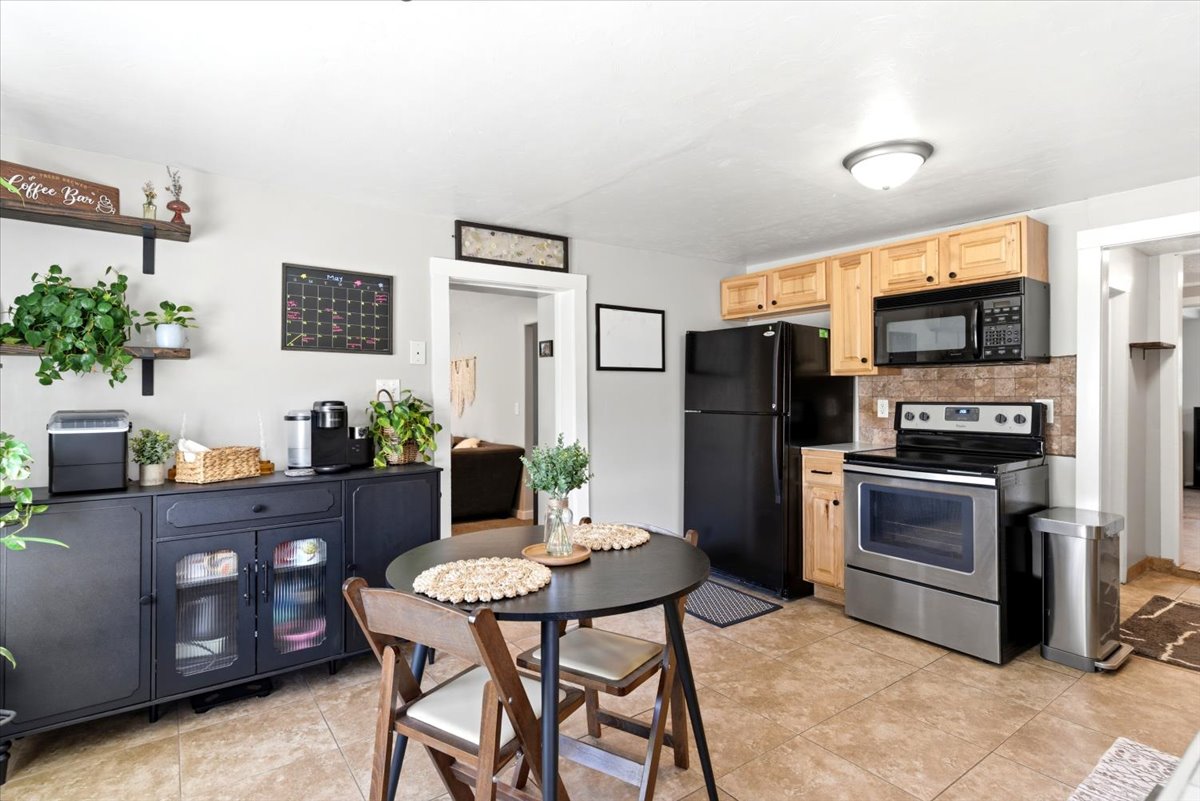 Kitchen featuring wood cabinetry, a stainless steel range with overhead microwave, a black refrigerator, and a tiled backsplash