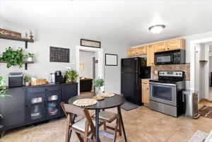Kitchen featuring wood cabinetry, a stainless steel range with overhead microwave, a black refrigerator, and a tiled backsplash