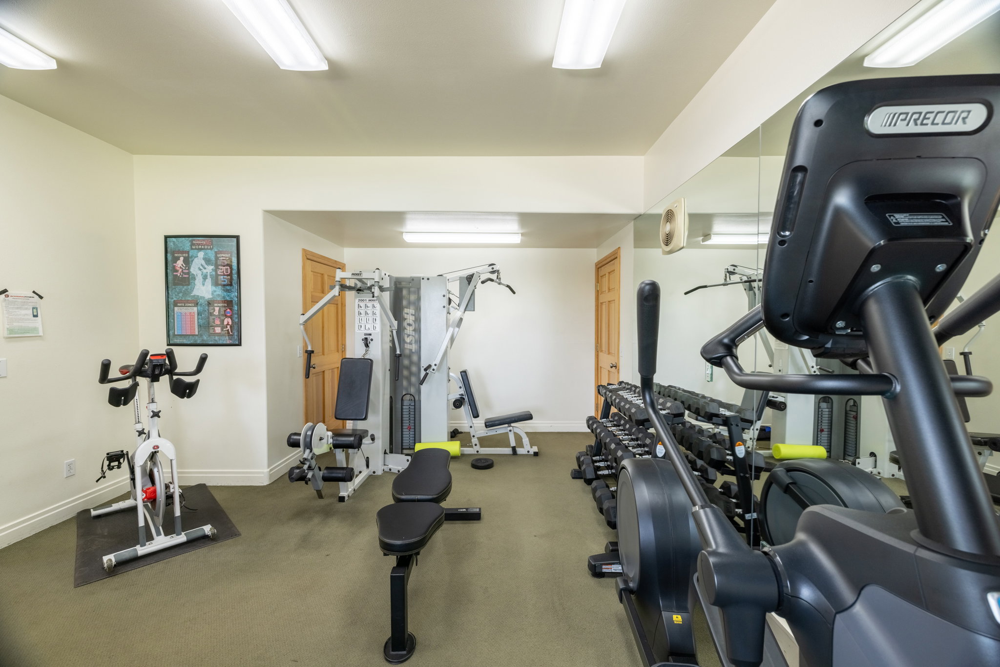 Dedicated fitness area featuring wall-to-wall mirrors, task lighting, wood-finish doors, and low-pile carpet flooring
