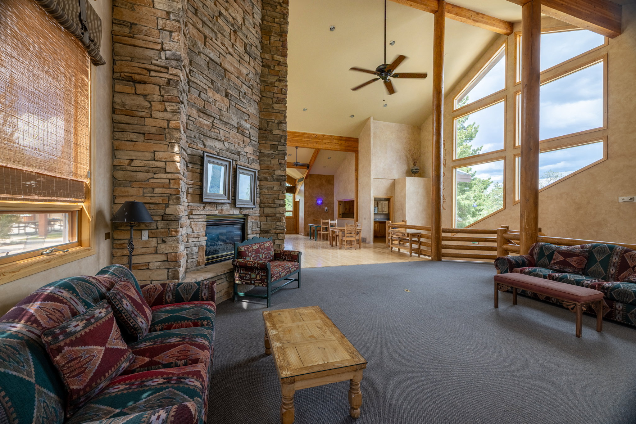 Spacious living area featuring a floor-to-ceiling stone fireplace, vaulted ceilings with exposed wood beams, and a ceiling fan
