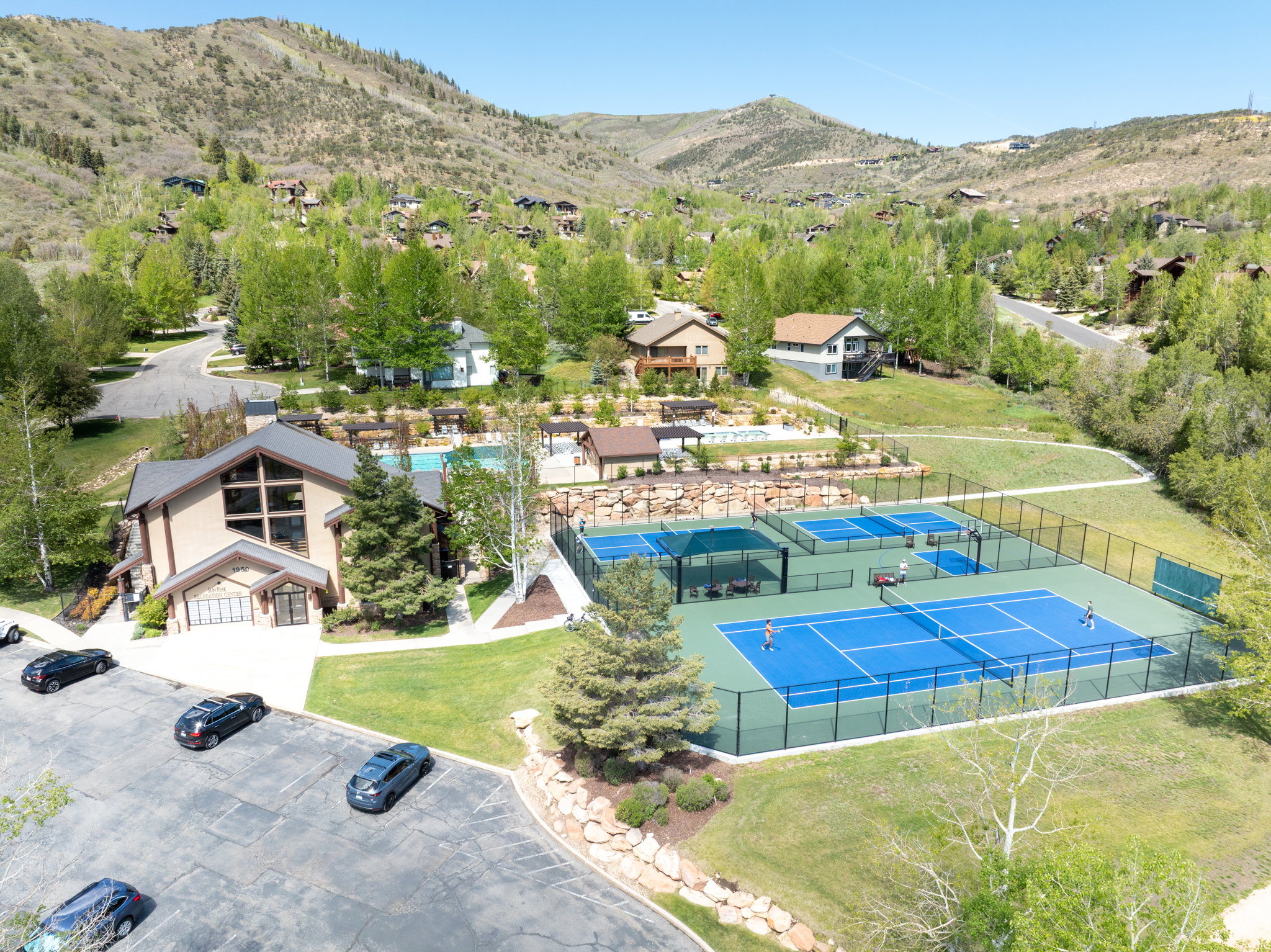 Recreational complex featuring multiple tennis/pickleball courts, a large swimming pool, and a multi-story clubhouse