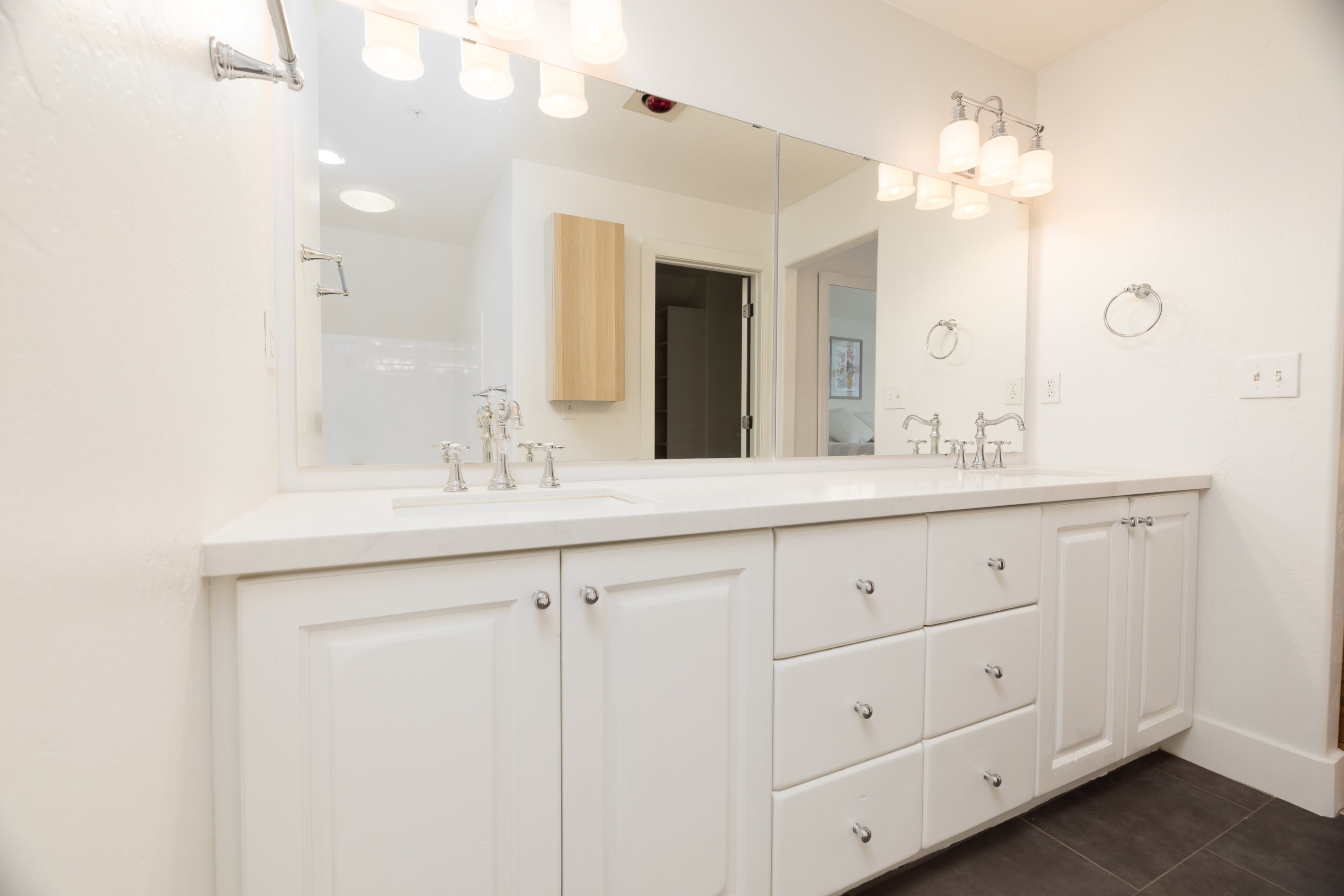 Dual vanity with white shaker-style cabinetry, chrome hardware, and a light-toned countertop