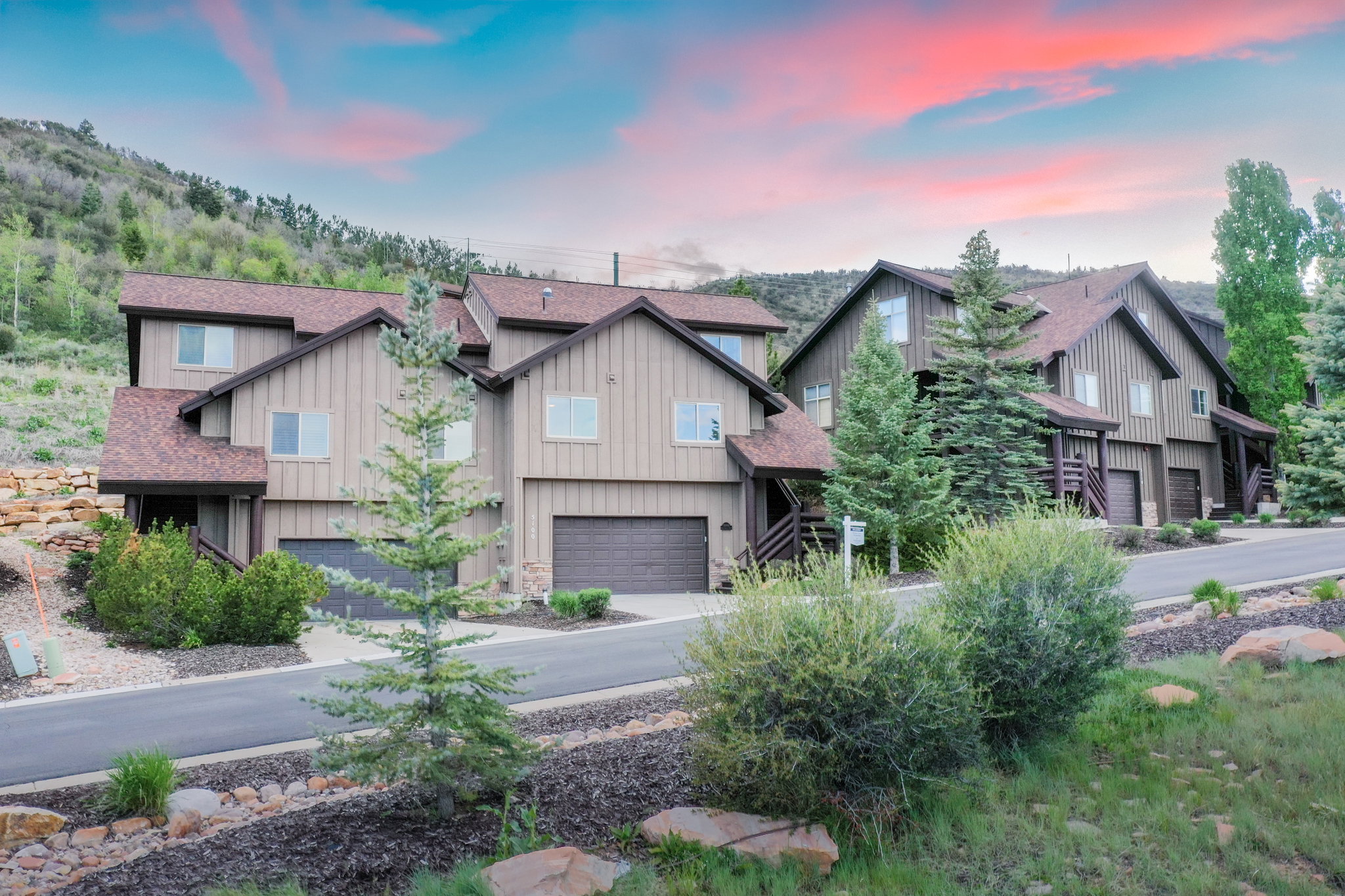 Multi-level townhome featuring a neutral vertical siding facade, attached garage, and prominent gable roofs