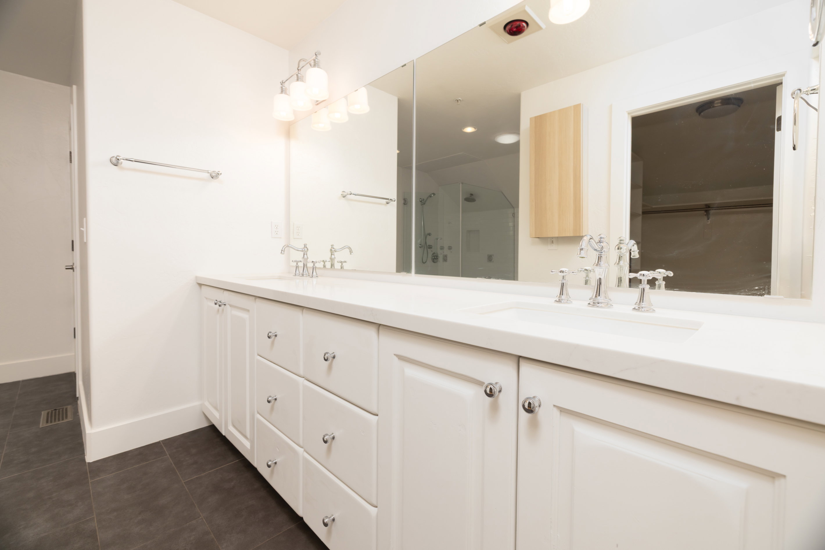 Double vanity with white cabinetry, integrated sinks, chrome fixtures, and a large wall-mounted mirror