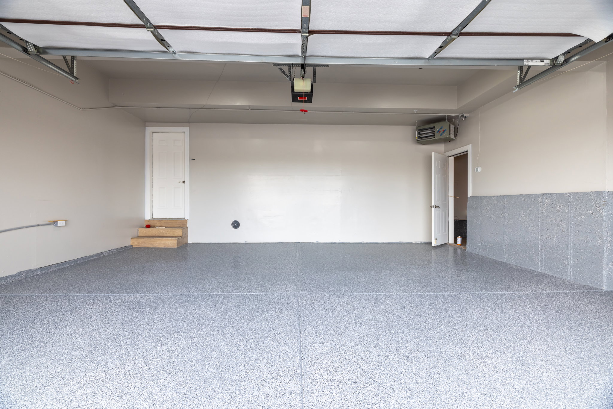 Spacious garage featuring a speckled epoxy flooring, painted walls, two access doors, and an overhead garage door mechanism
