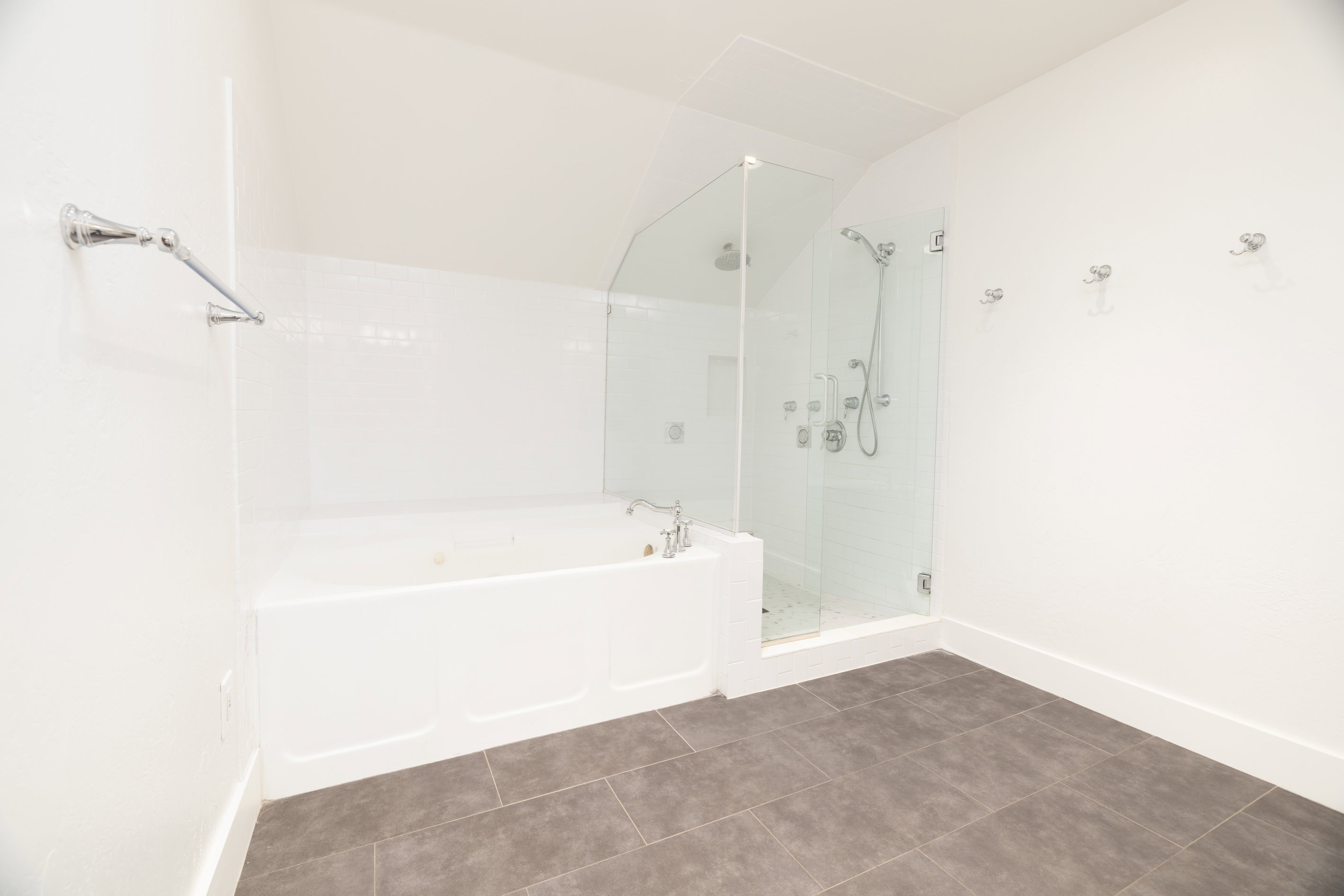 White-tiled bath and glass-enclosed shower with multiple shower heads